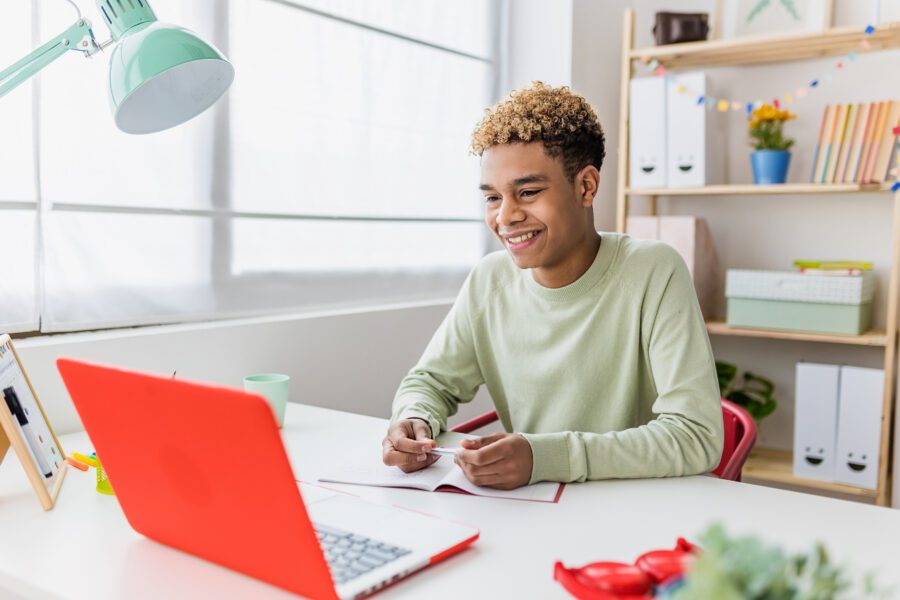 Smiling teenager boy studying online from home having a video conference on laptop with school teacher - Education and learning online concept