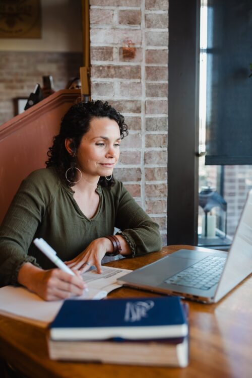 a woman writing in a notebook and working at a laptop